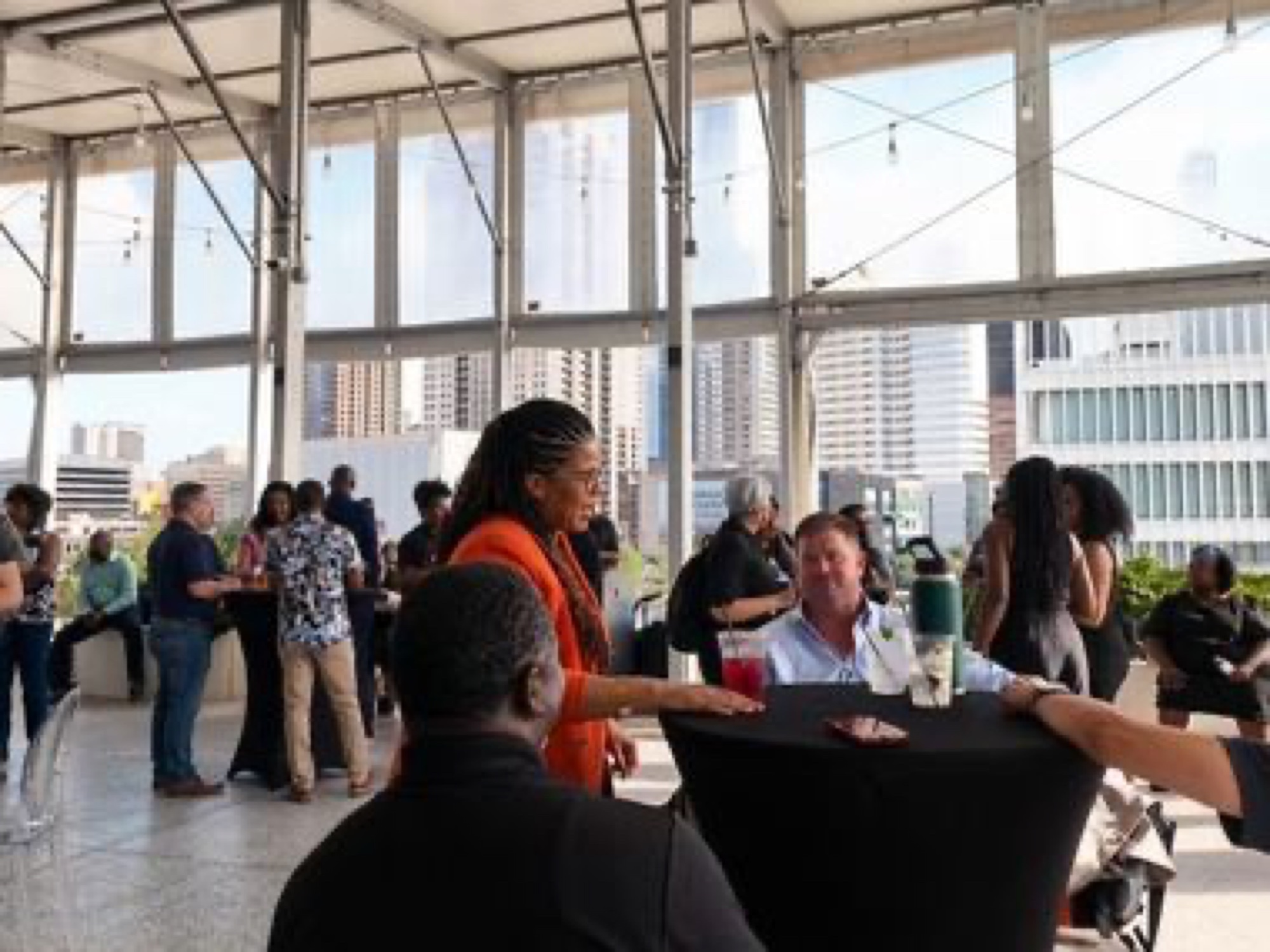 Attendees mingling at standing tables during the rooftop reception, with downtown Houston towers through the windows