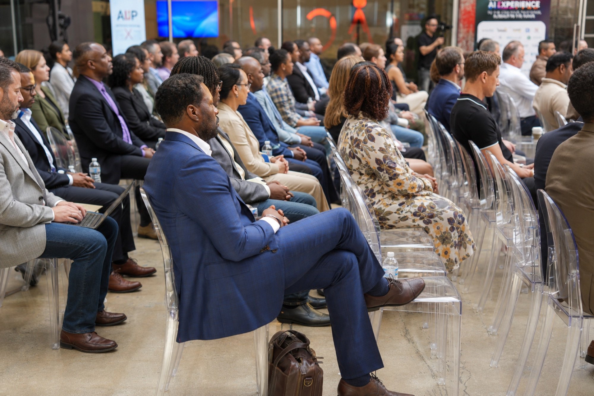A seated audience on clear chairs listening to a session