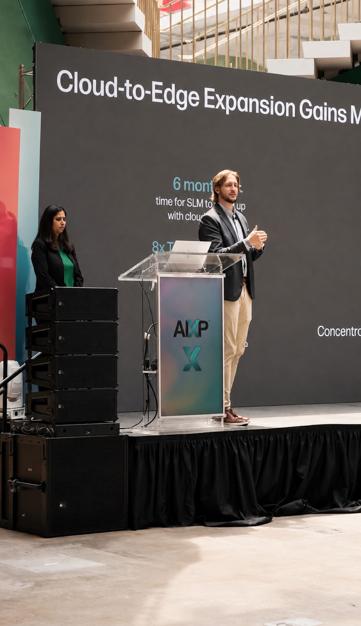 A speaker presenting on stage beside a slide titled Cloud-to-Edge Expansion, with a moderator at the podium