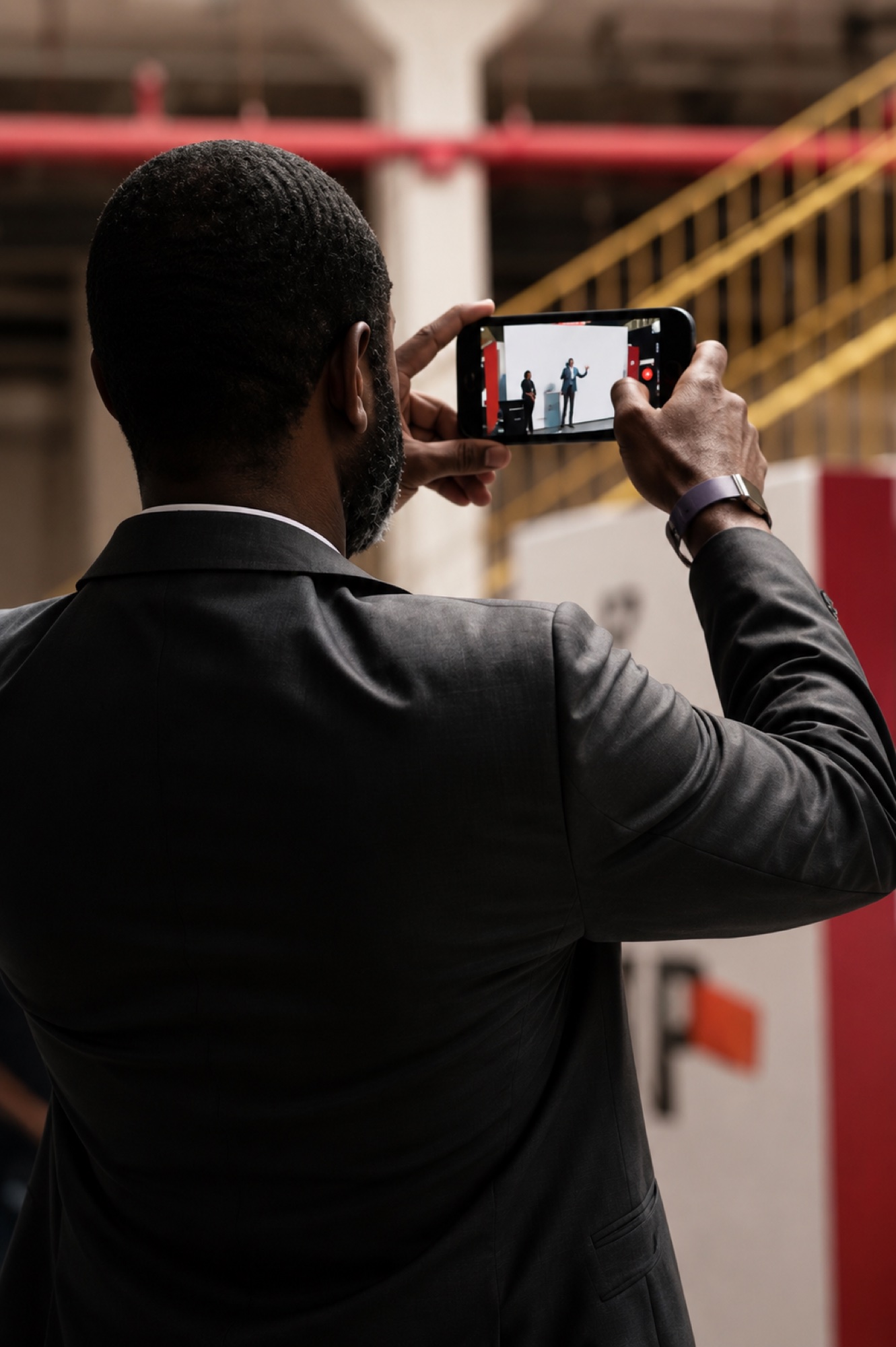An attendee in a suit filming the main stage on his phone from the audience