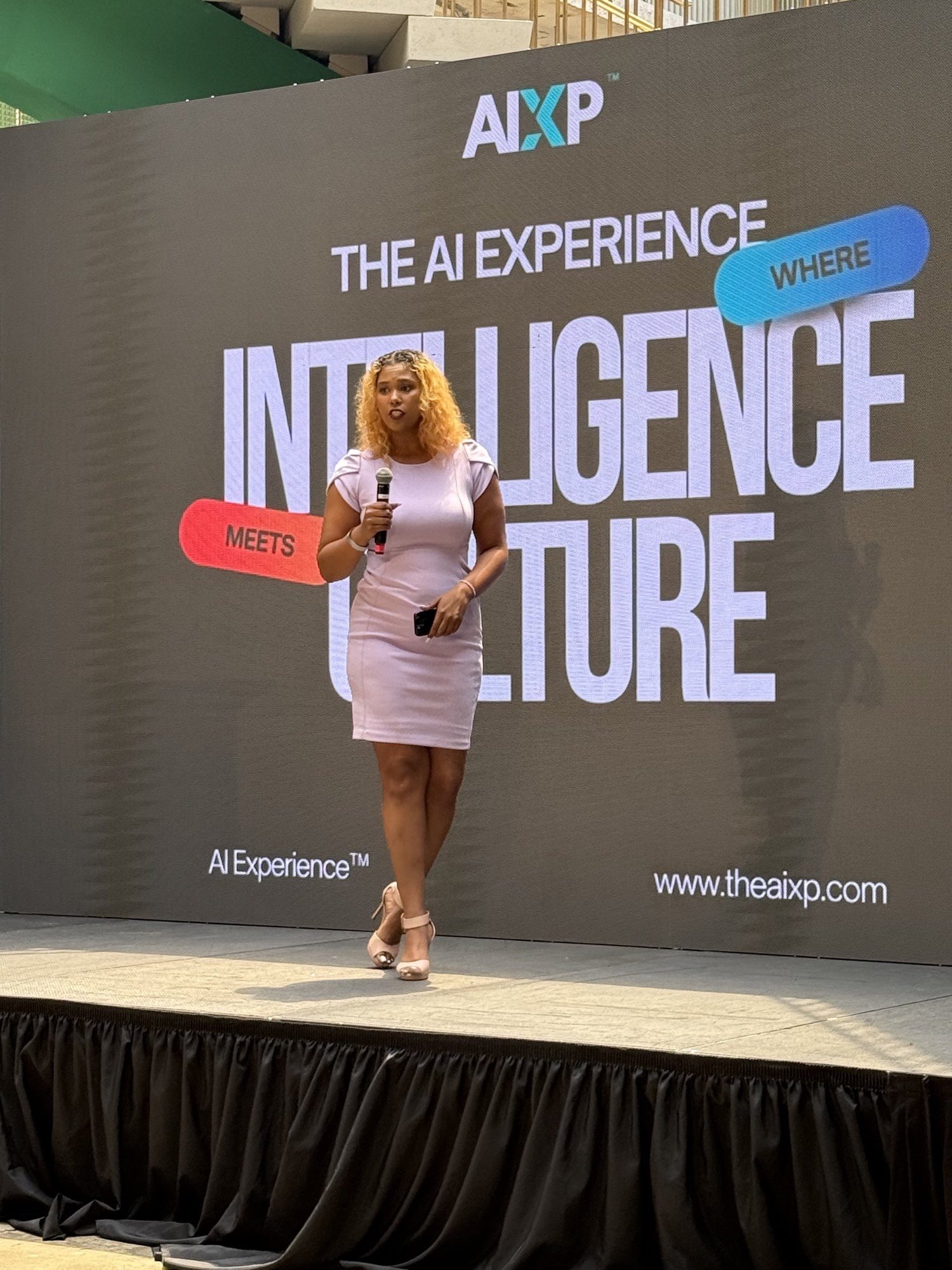 A speaker holding a microphone on the main stage in front of the Where Intelligence Meets Culture backdrop